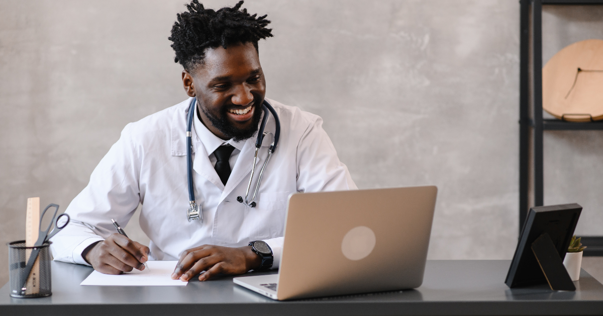 Doctor smiling while looking at laptop and taking notes
