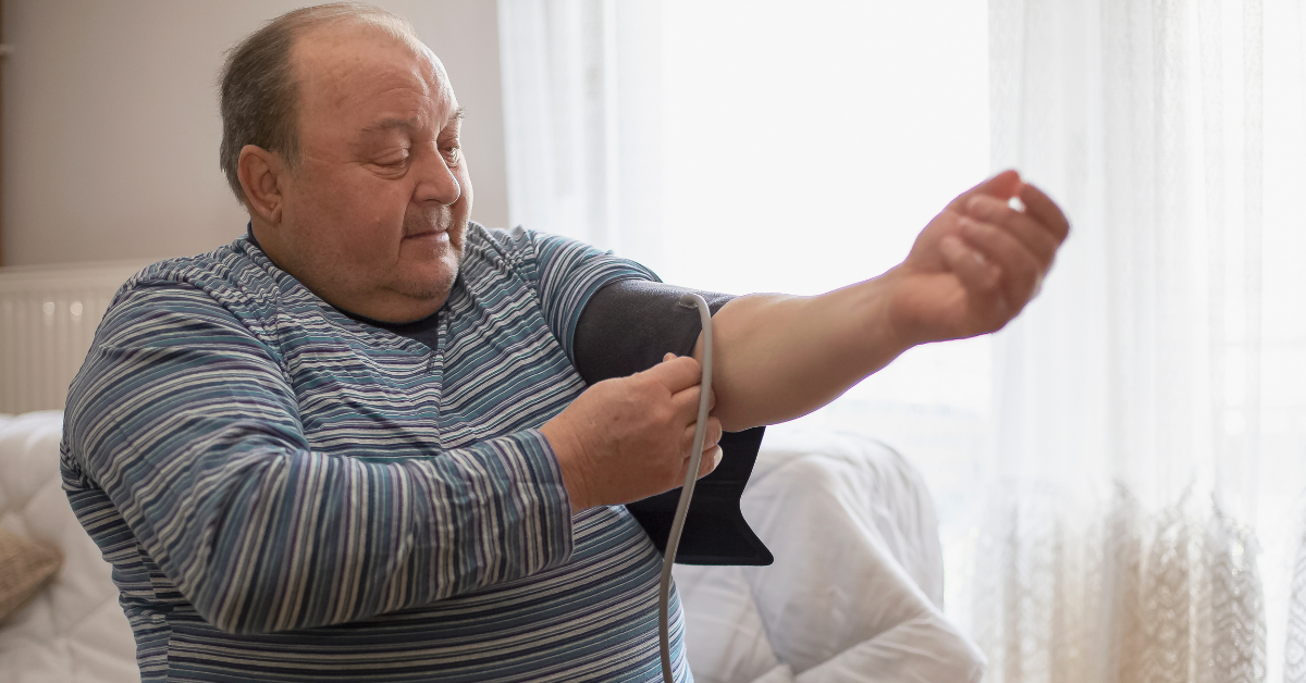 Man sitting at home putting blood pressure cuff on arm